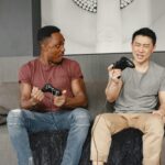 Two men enthusiastically playing video games on a couch, showcasing friendship and fun.