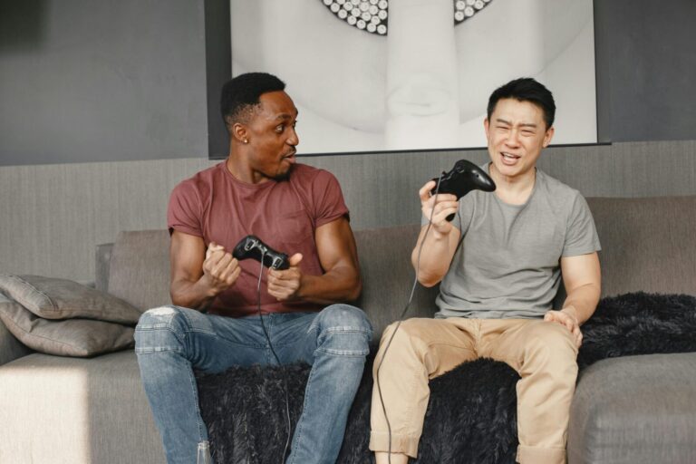 Two men enthusiastically playing video games on a couch, showcasing friendship and fun.