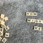 Scrabble tiles spell out "how might we" on carpet.